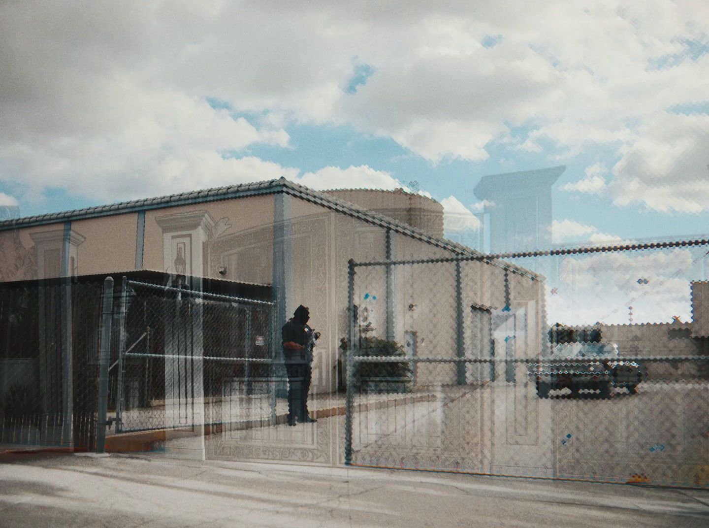 a man standing in front of a building behind a chain link fence