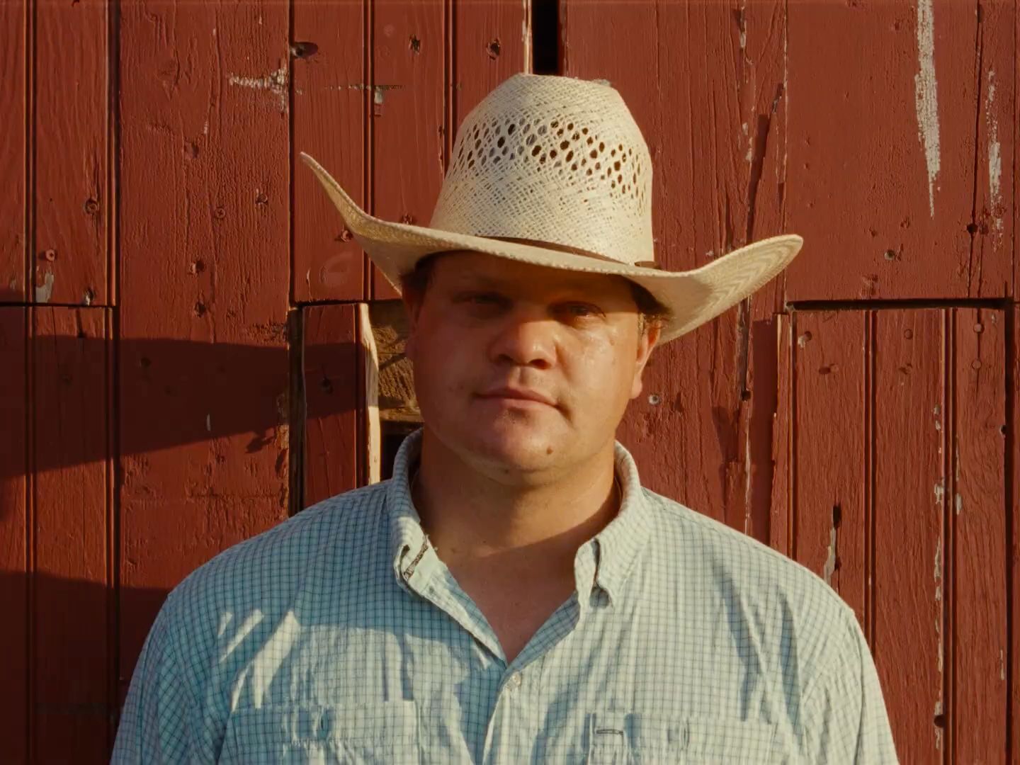 a man wearing a cowboy hat standing in front of a red barn