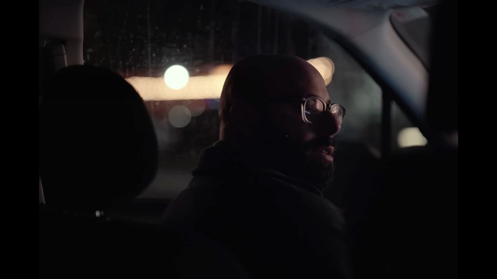 a man with glasses sitting in a car at night