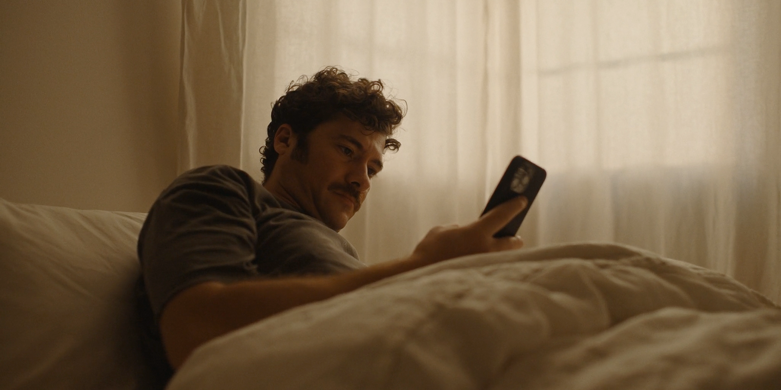 a man laying in bed looking at a cell phone