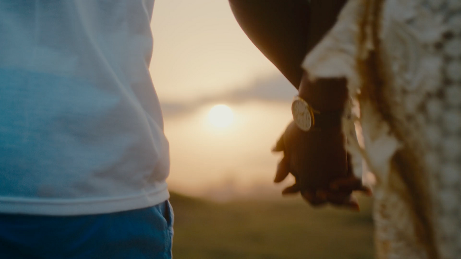 two people holding hands with the sun setting in the background