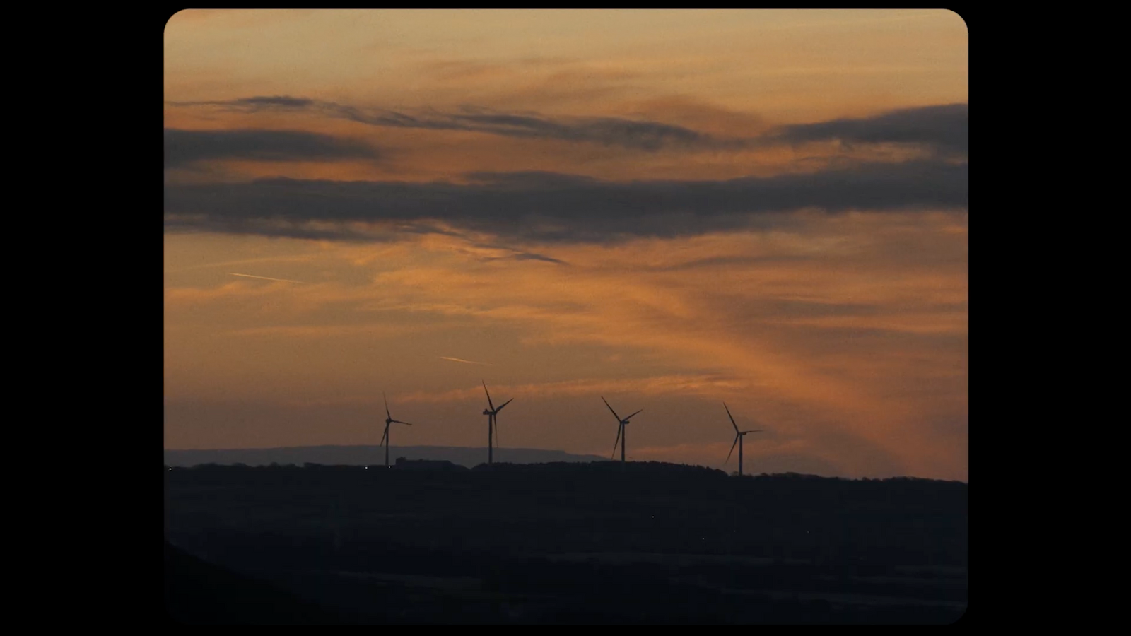 a group of windmills on a hill at sunset