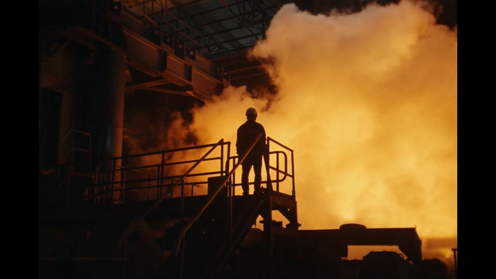 a man standing in front of a factory filled with smoke