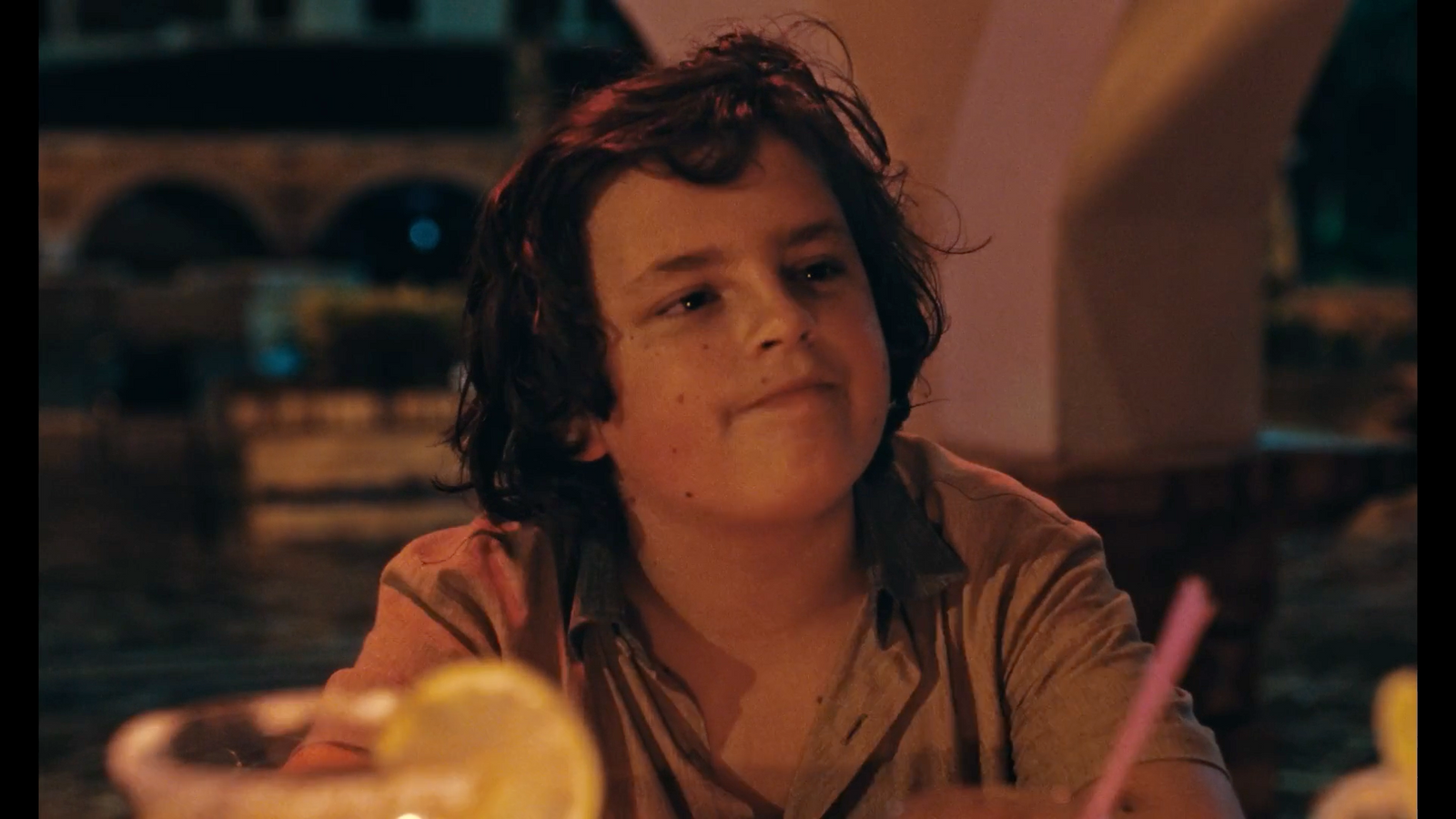 a young boy sitting at a table with a drink