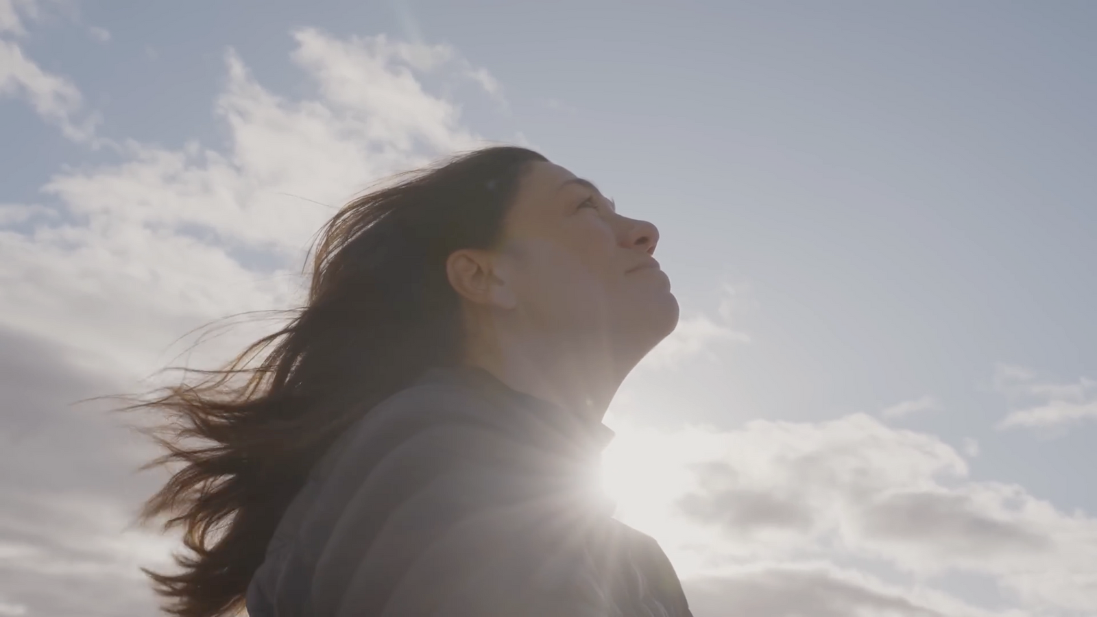 a woman looking up into the sky with her hair blowing in the wind