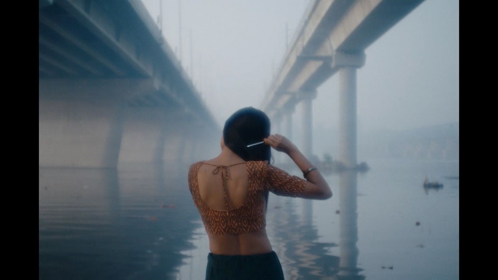 a woman standing in the water looking at a bridge
