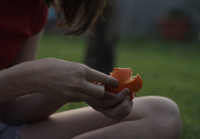 a person sitting in the grass peeling an orange