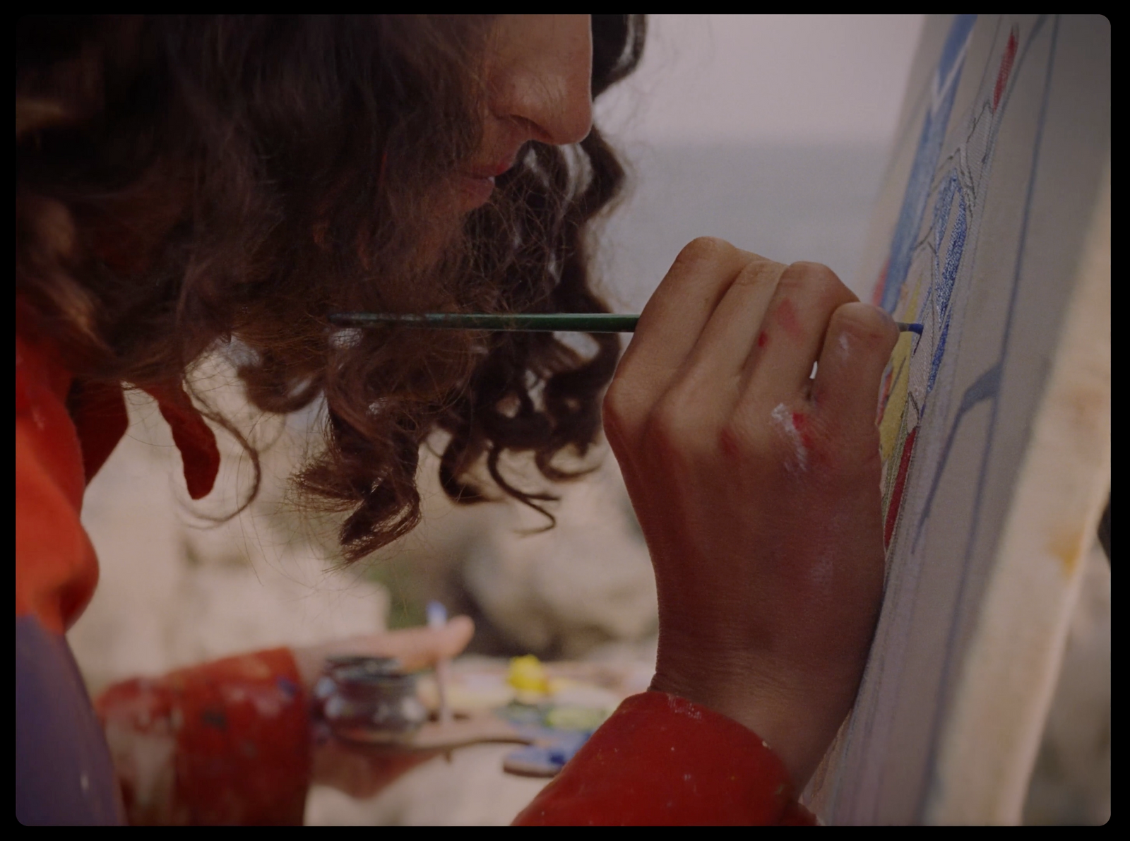 a man with long curly hair painting on a canvas