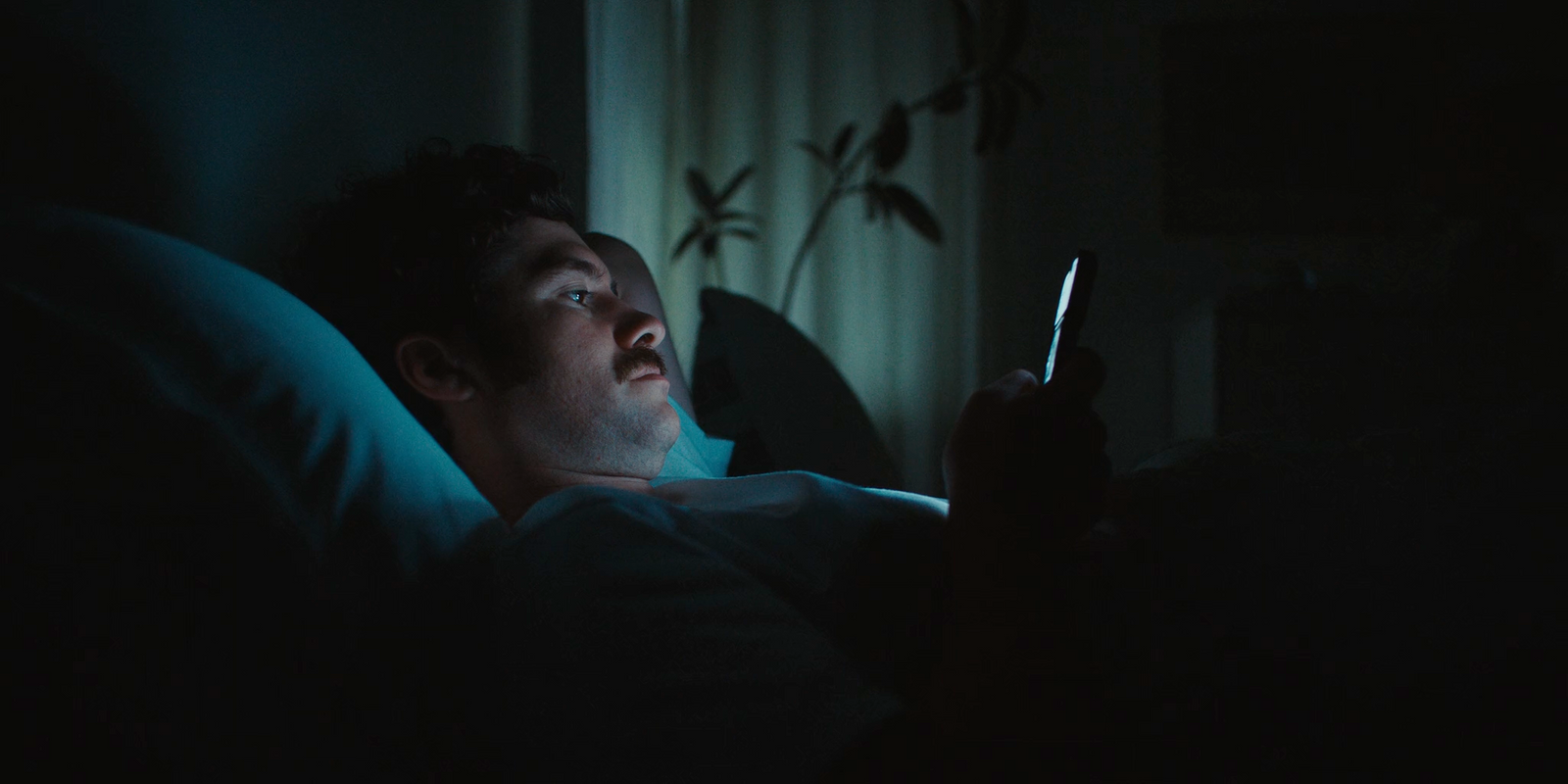 a man laying in bed looking at a cell phone