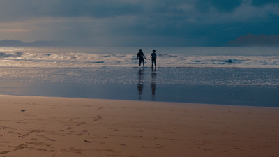 a couple of people standing on top of a sandy beach