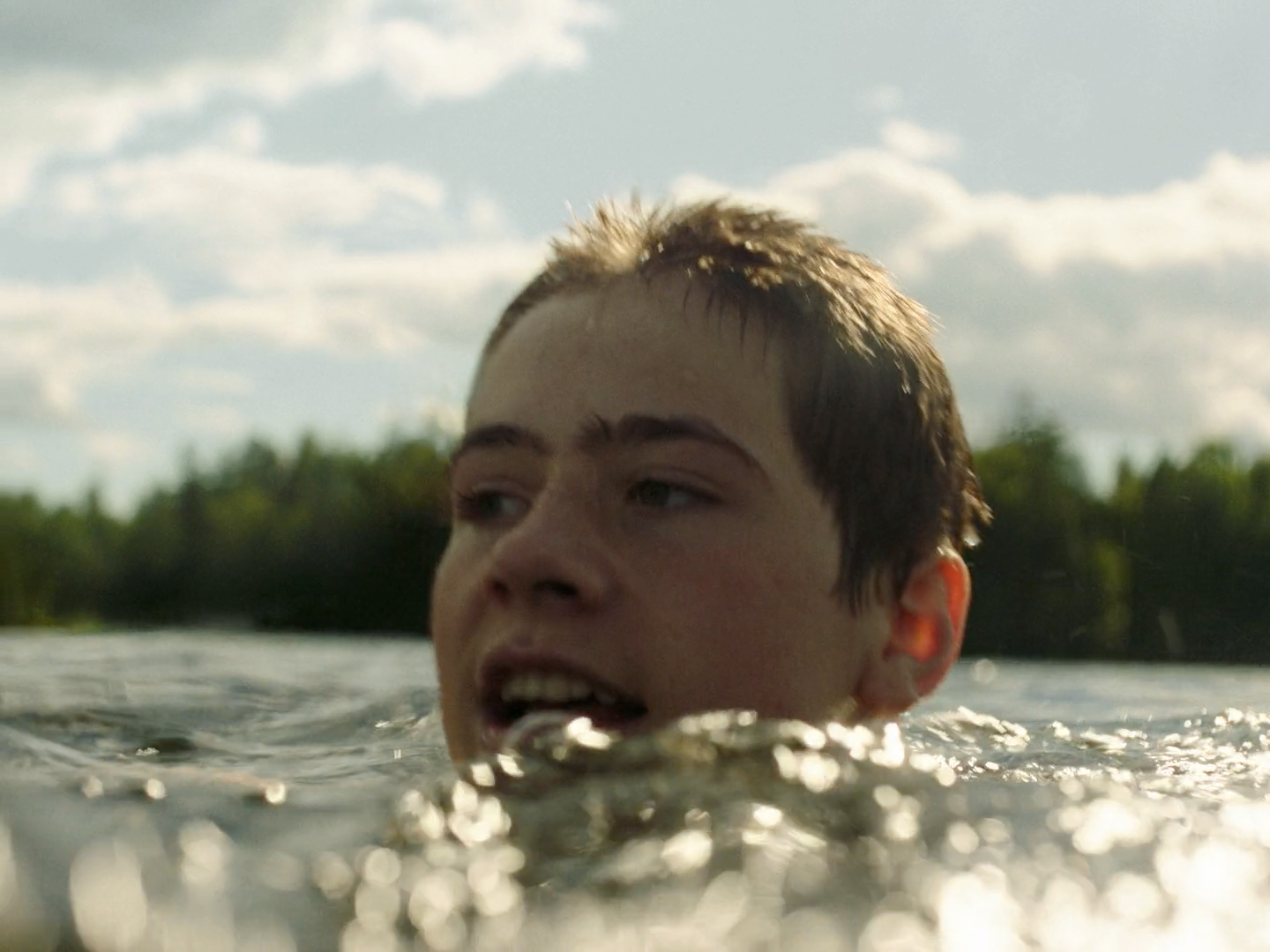 a boy swimming in a lake with trees in the background