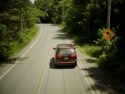 a red car driving down a road next to a forest