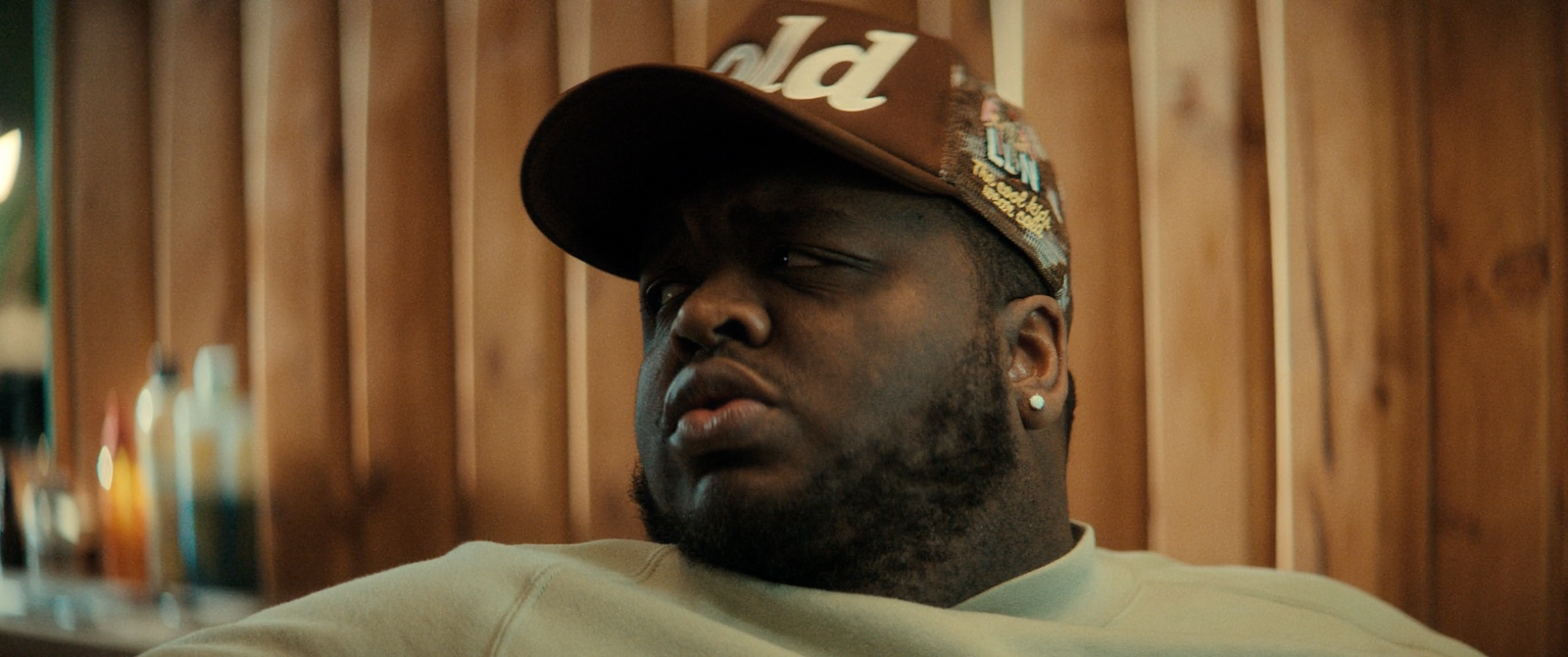 a man wearing a hat sitting in front of a wooden wall