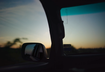 a rear view mirror of a car with a sunset in the background