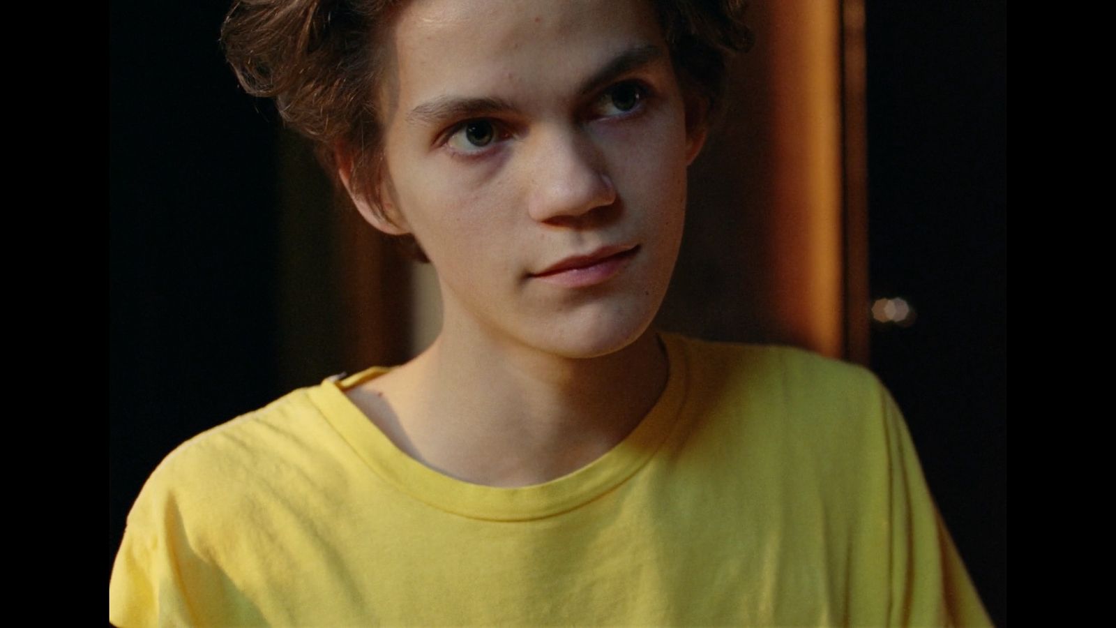 a boy in a yellow shirt looking at the camera