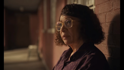 a woman wearing glasses standing next to a brick wall