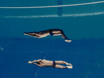 a man dives into a pool while another swims in the water