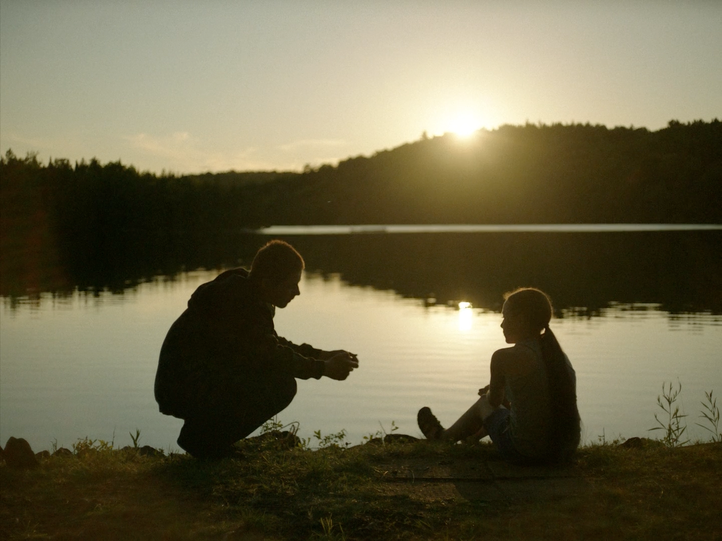 a man and a woman sitting on the ground next to a lake