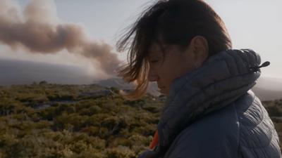 a woman standing in a field with a lot of smoke coming out of her mouth