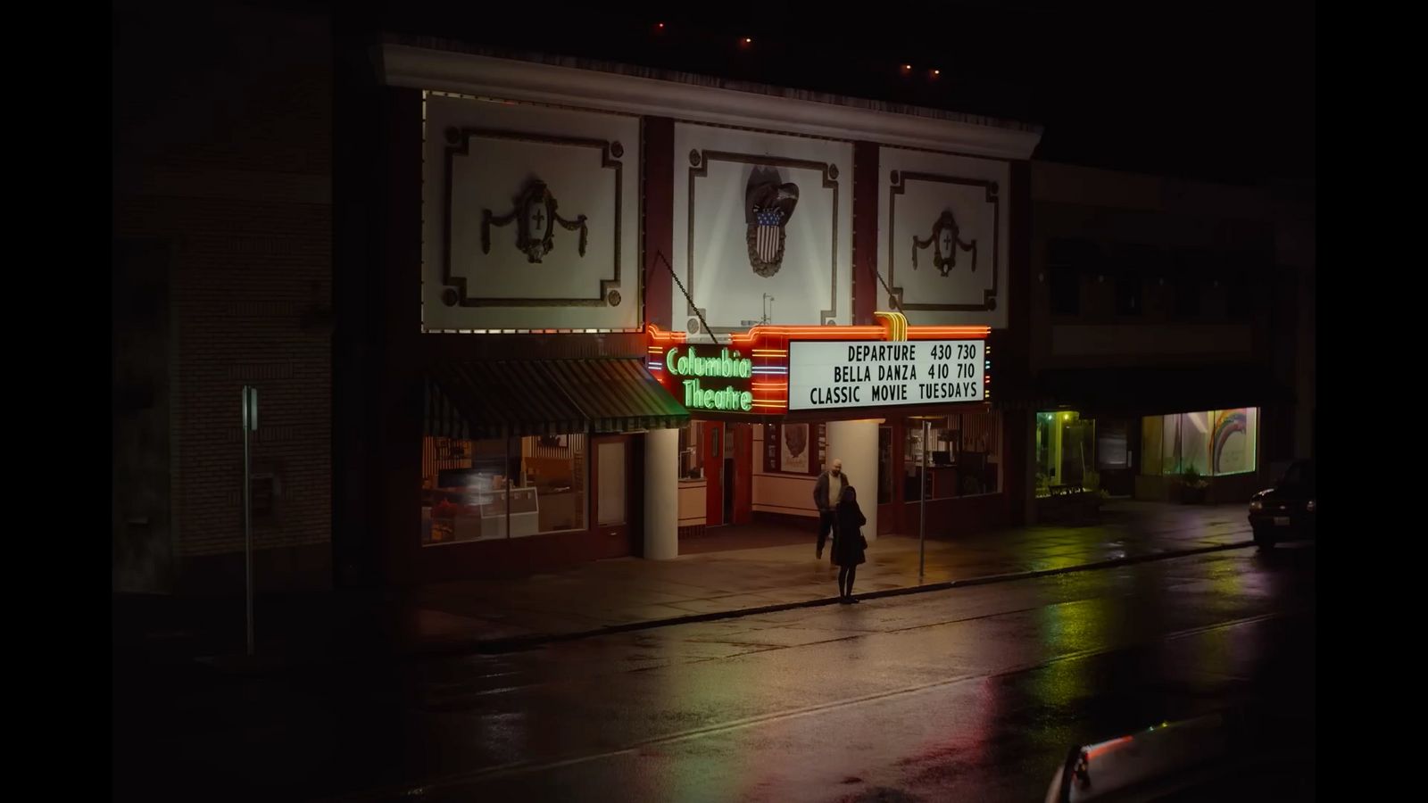 a person walking down a street in front of a theater