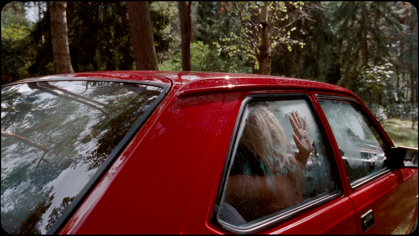 a woman waving out of a red car window