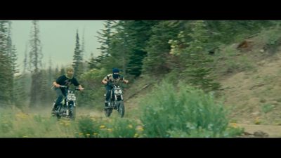 a couple of people riding motorcycles down a dirt road