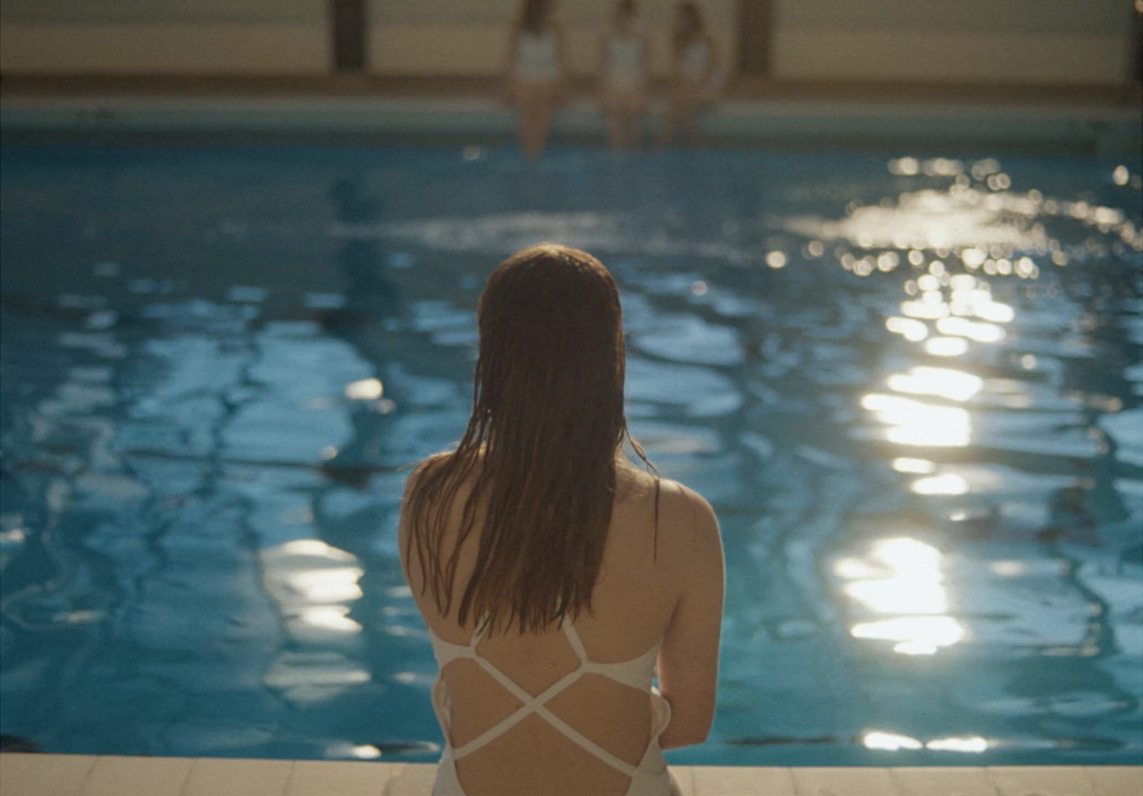 a woman in a white swimsuit sitting on a ledge next to a swimming pool