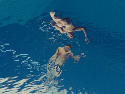 a man swimming in a pool with his reflection in the water