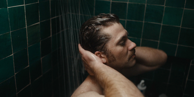 a man taking a shower in a green tiled bathroom