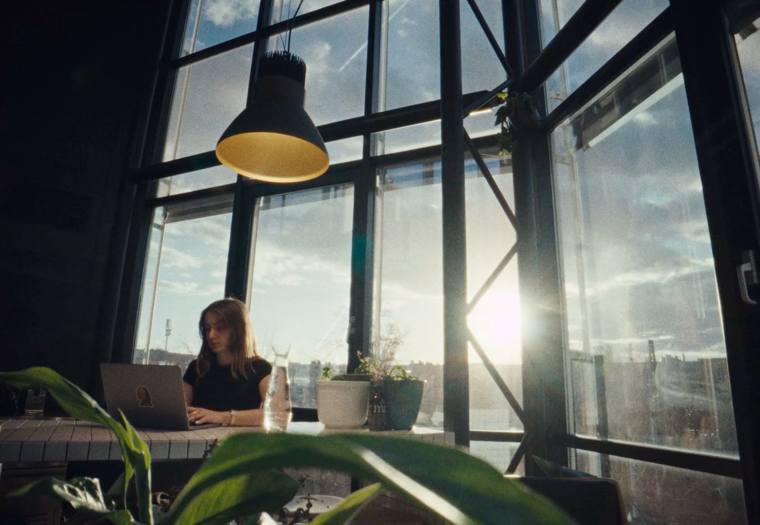 a woman sitting at a table with a laptop in front of a window