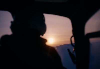 a person sitting in a vehicle looking out the window at the sunset