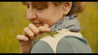 a woman in a field with a lizard on her shoulder