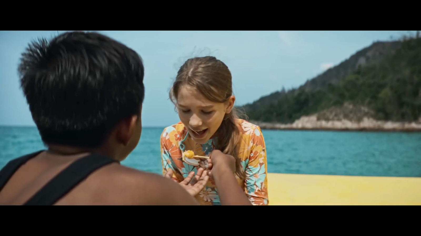 a young girl eating a piece of food next to a man