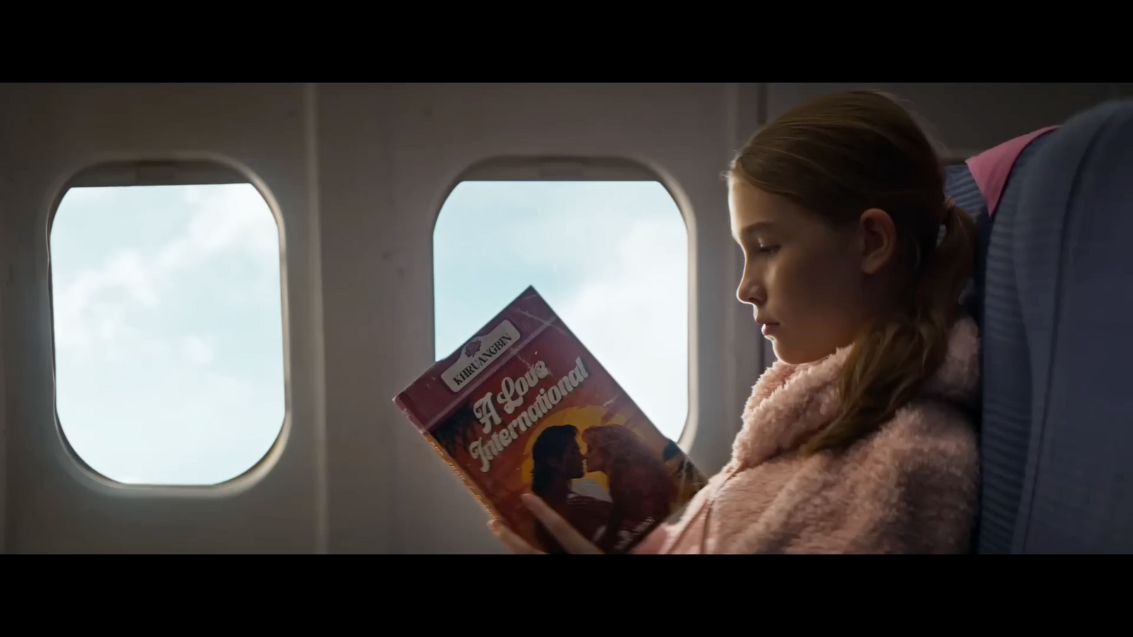 a little girl sitting on an airplane reading a book