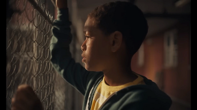 a young boy standing next to a chain link fence