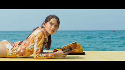 a young girl laying on the beach reading a book