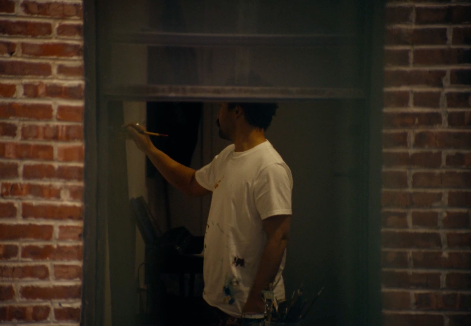 a man in a white t - shirt is looking out a window