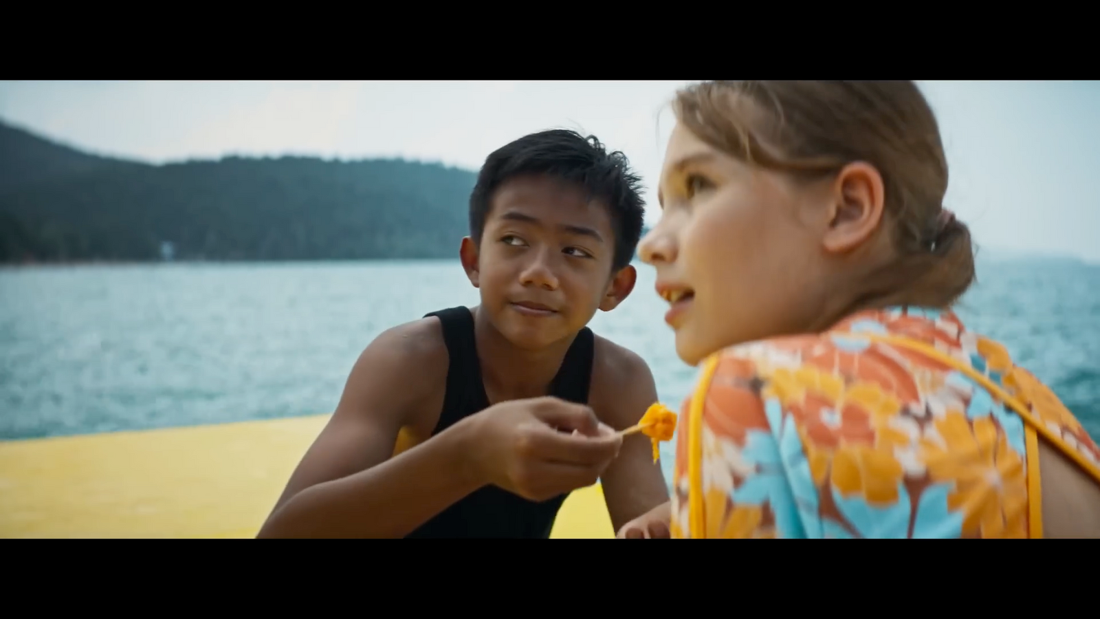 a boy and a girl eating food by the water