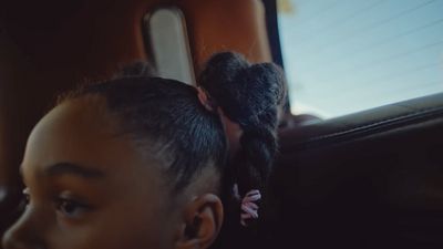 a young girl sitting in a car with her hair in a pony tail