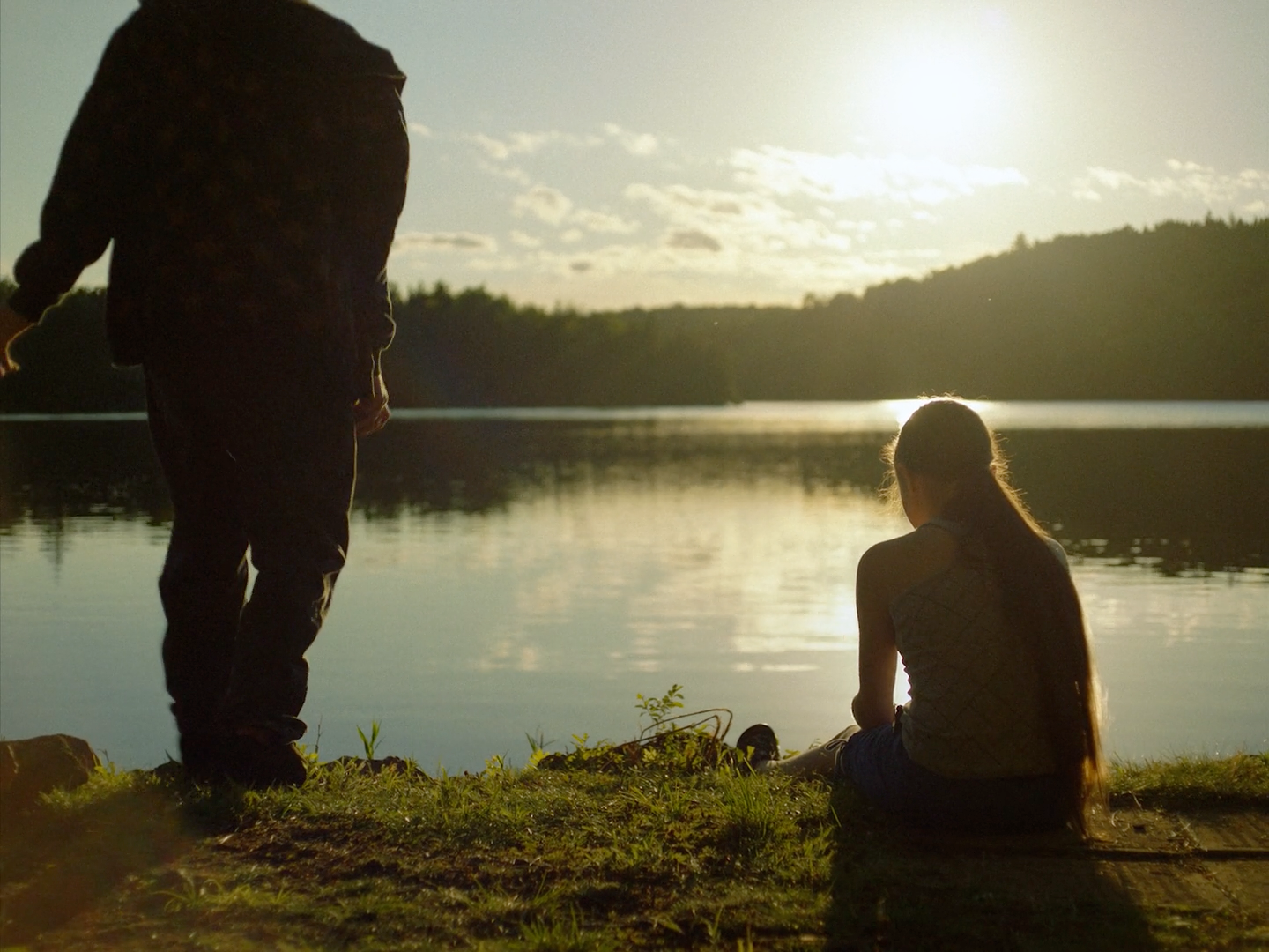 a man and a woman sitting on the grass near a body of water