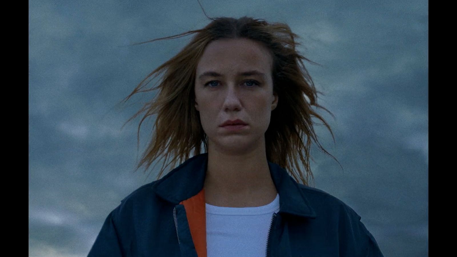 a woman with long hair standing in front of a cloudy sky