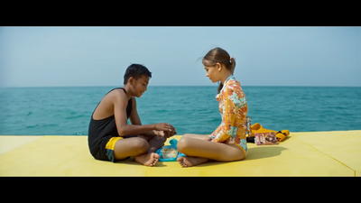 a man and a woman sitting on the ground next to the ocean