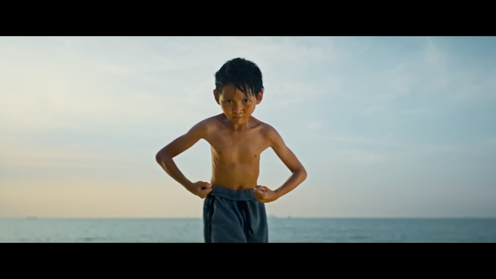 a young boy standing on the beach with his hands on his hips