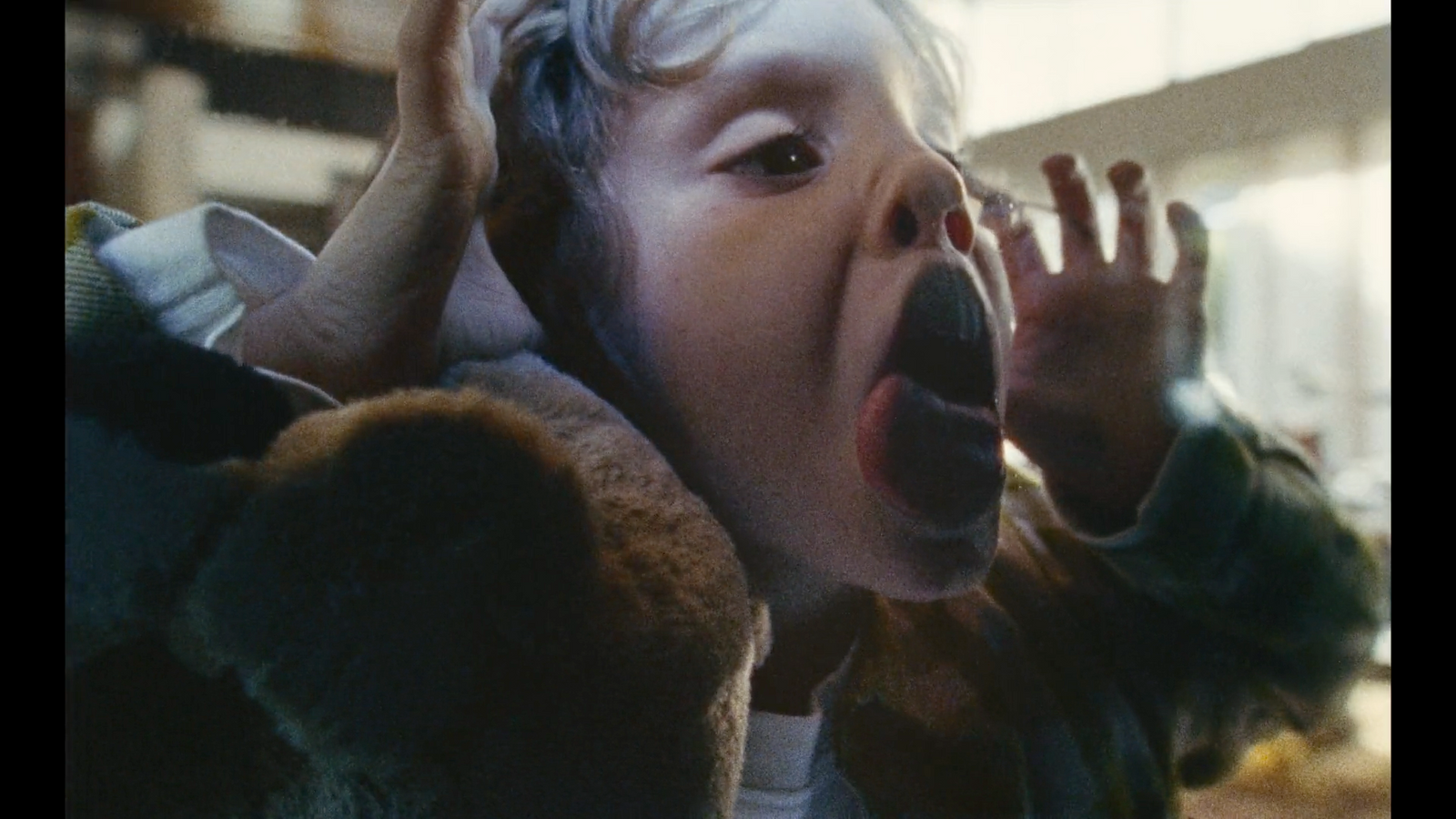 a young boy holding his hands up to his ears