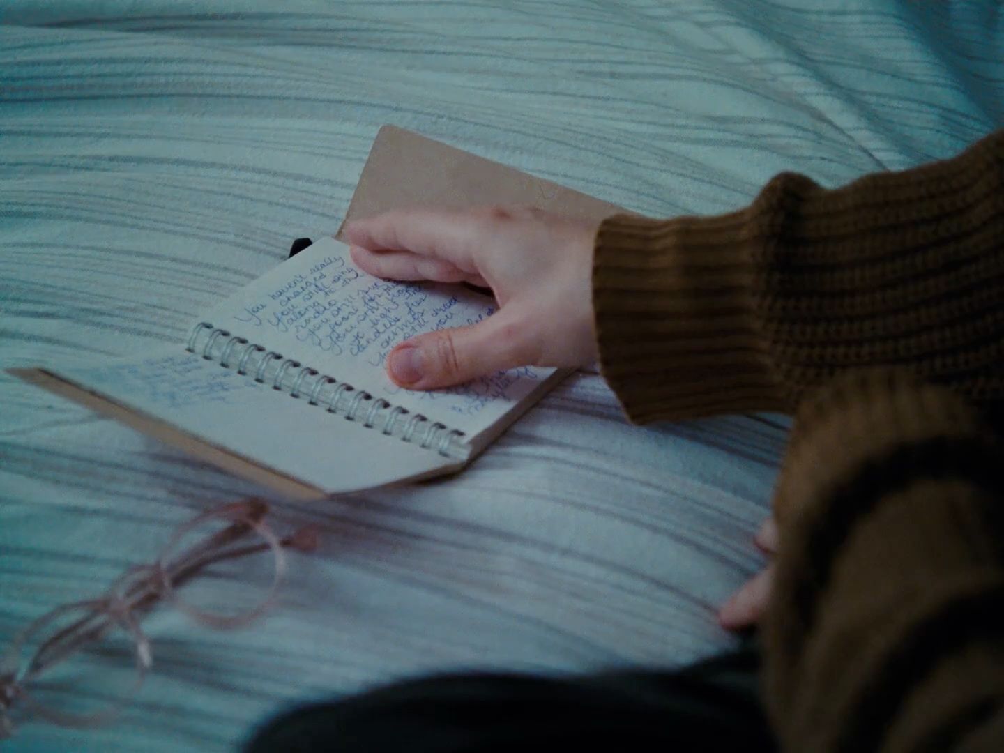 a person writing on a notebook on a bed