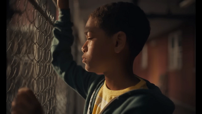 a young boy is looking through a chain link fence