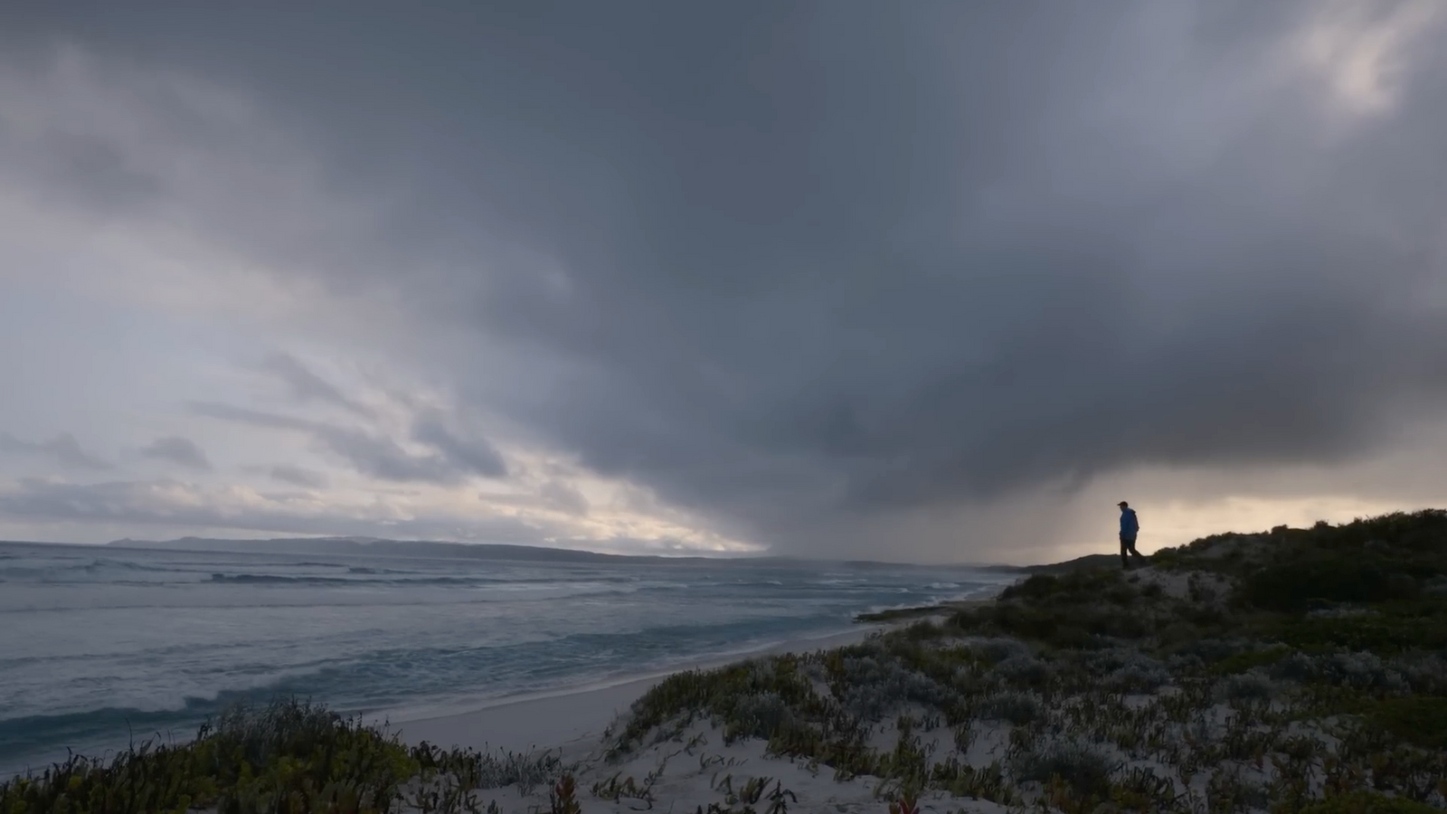 a man standing on top of a sandy beach under a cloudy sky