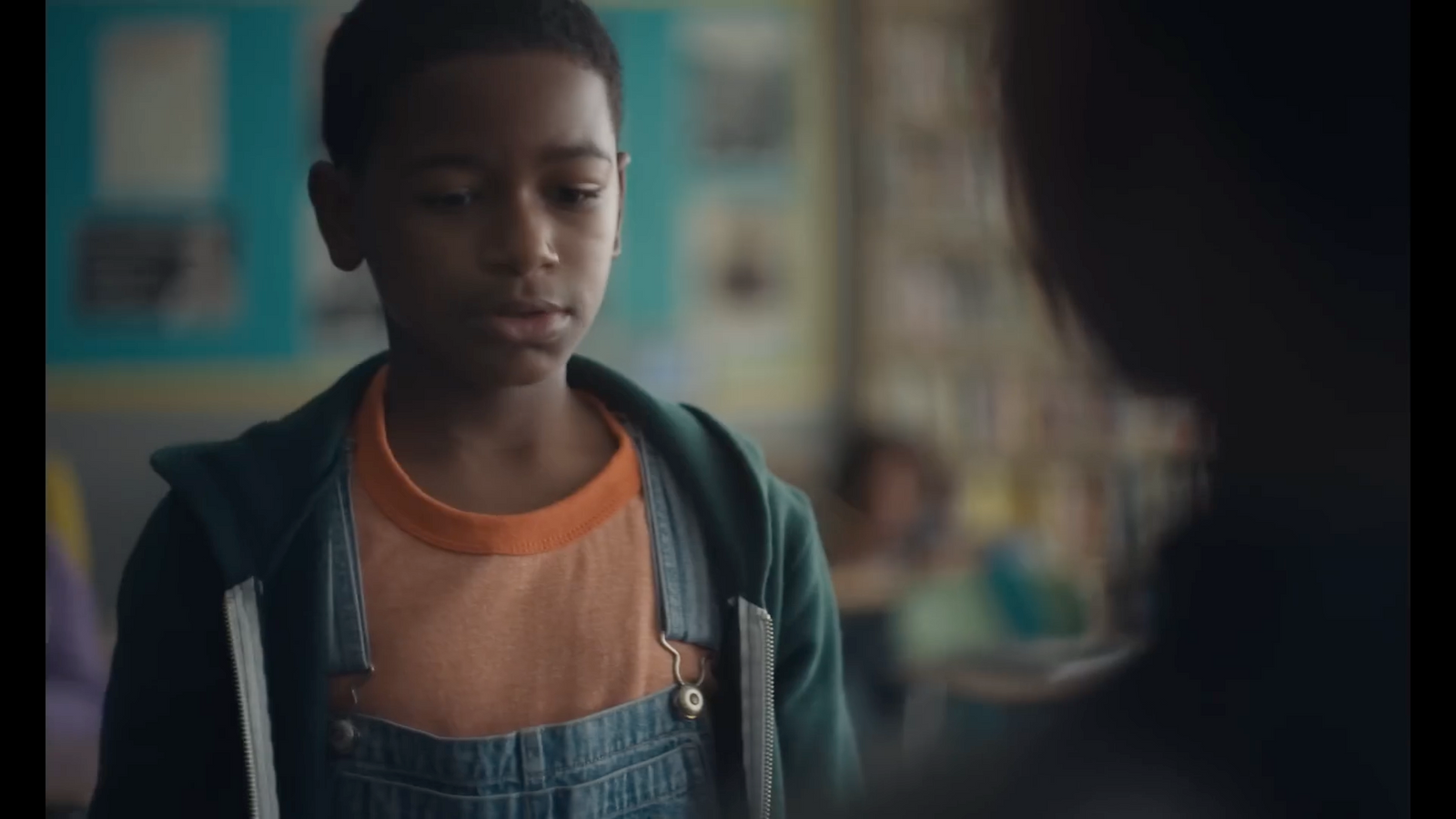 a young boy in overalls standing in a room