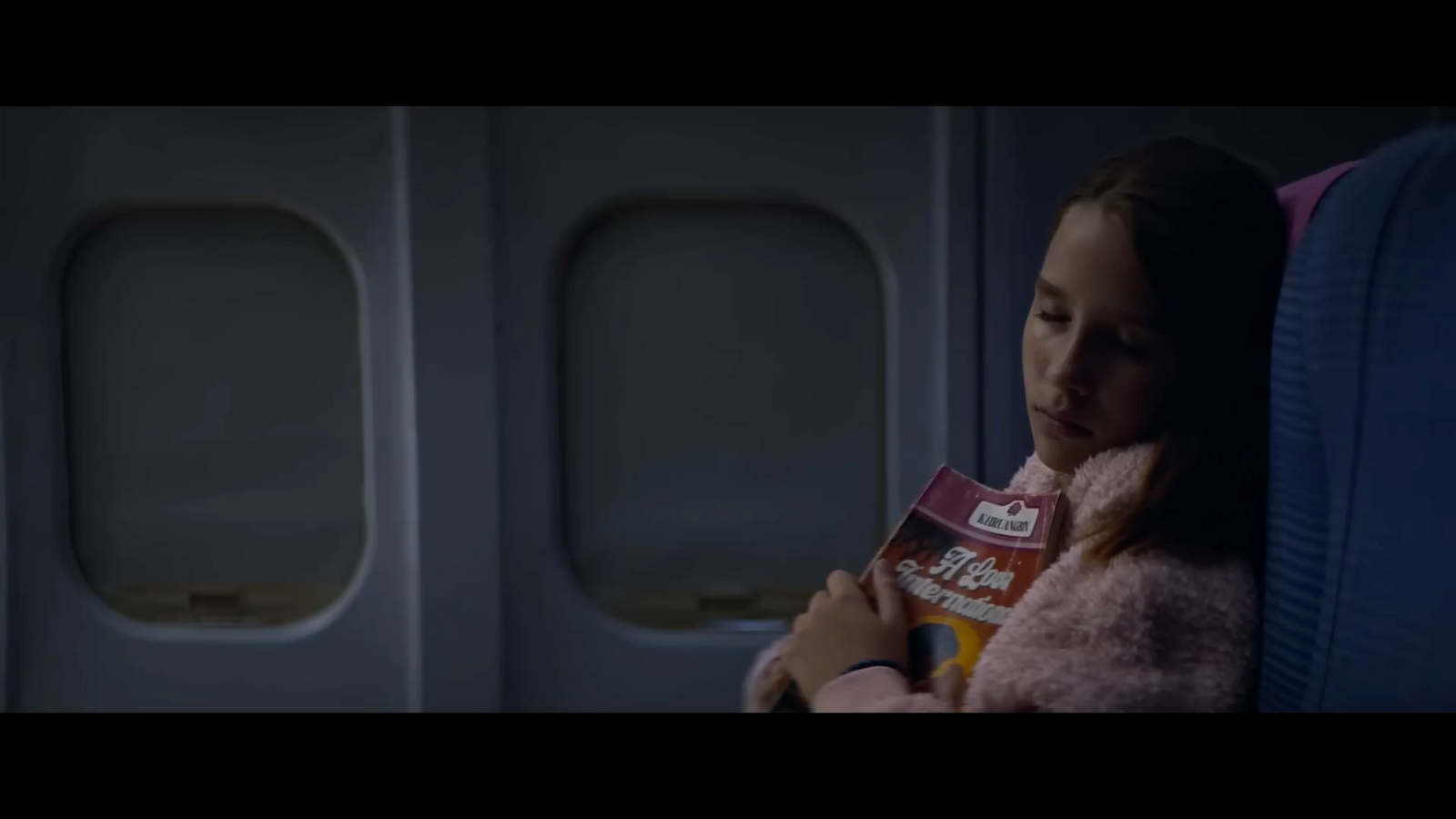 a girl sitting on an airplane reading a book