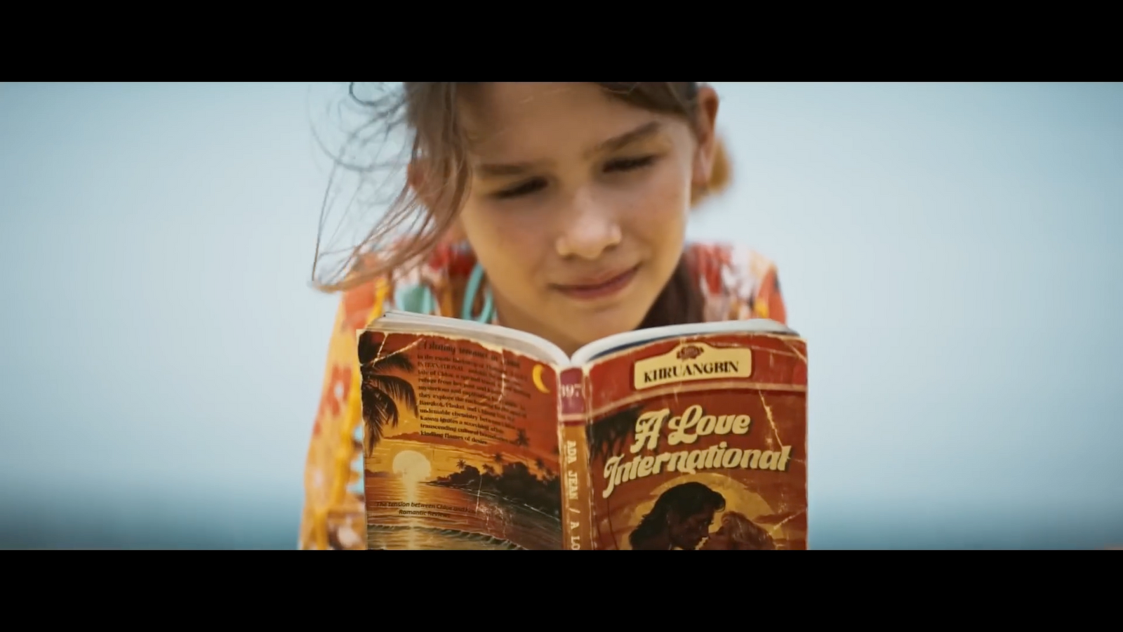 a young girl reading a book on the beach